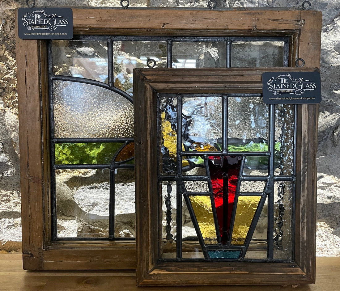 A pair of early 20th century antique stained glass panels, one in front of the other and showing ambers, greens and some lovely red.